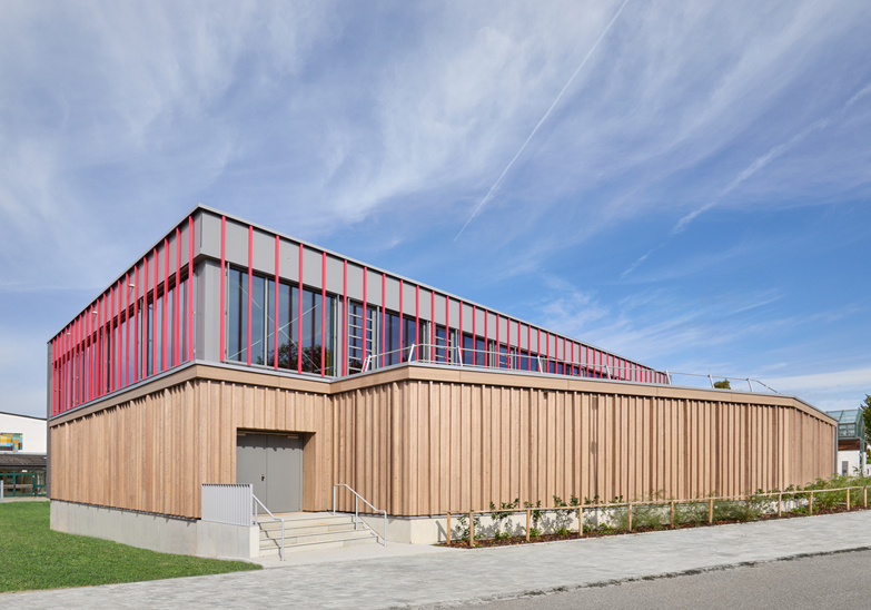Neue Sporthalle in Kösching mit Holzfassade und roten Farbakzenten